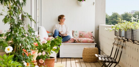 A woman sitting on a bench, surrounded by plants on a balcony.
