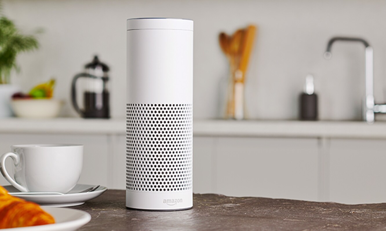 White Amazon voice assistant smart device sitting on a kitchen counter.
