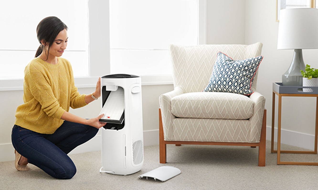 Woman kneeling next to a corner chair in a room changing out the True HEPA filter.
