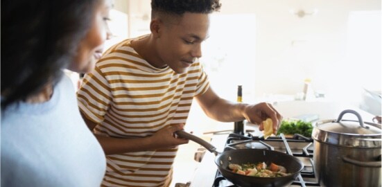 A boy squeezing a lemon into a pan, with his mother in the foreground.
